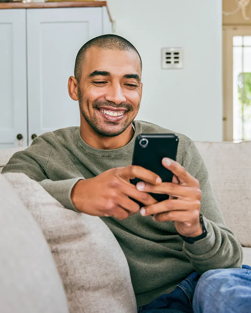 Man On Couch Looking At Phone Smiling